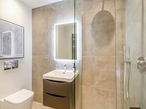 Et moderne badeværelse med glasbrusekabine, et hvidt håndvaskskab med spejl over, samt et toilet.