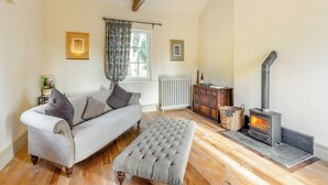Ein gemütliches Wohnzimmer mit Sofa, Hocker, Kamin und Holzbalken an der Decke.