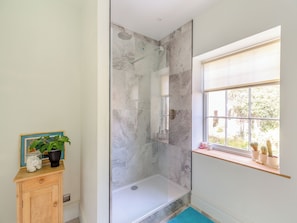A modern bathroom with a glass-enclosed shower, marble walls, a wooden vanity, and a window with a view of greenery. - Apartment at Llanerchydol Hall (Welshpool)