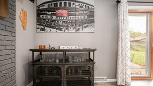 A room with a vintage baseball poster, a metal cabinet with glassware, and a view through a window with curtains. - Golden Shamrock<>3BR Home 3min to ND (South Bend)
