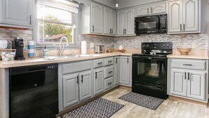 A modern kitchen with grey cabinets, a black microwave, and a dishwasher. - Golden Shamrock<>3BR Home 3min to ND (South Bend)