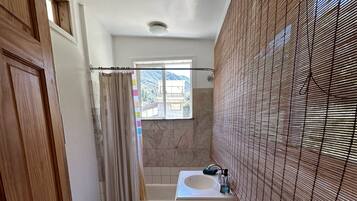 A bathroom with a wooden door, a window with a view of mountains, a bathtub, a sink, and a tiled floor.