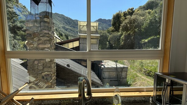 A kitchen with a stainless steel sink, a wooden rack, and a window overlooking a mountainous landscape. - Panoramic Loft with Deck, Private Trails and Creek (Topanga)