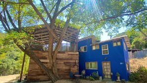 A two-story house with a wooden deck and a blue exterior. - Panoramic Loft with Deck, Private Trails and Creek (Topanga)