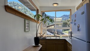 A kitchen with wooden cabinets, a built-in sink, and a refrigerator. There is a window with a view of mountains and a house. - Panoramic Loft with Deck, Private Trails and Creek (Topanga)