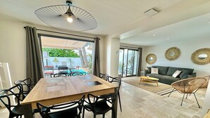A modern living room with a dining area, large windows, and a view of an outdoor pool. - Beautiful villa with private pool - heart of the village (La Flotte)