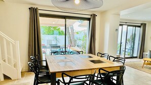 A dining area with a wooden table and black chairs, large windows with curtains, and a view of the outdoors. - Beautiful villa with private pool - heart of the village (La Flotte)
