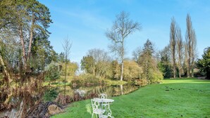 A serene outdoor setting with a grassy area, a small pond, and a white metal table with chairs.