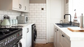 A compact kitchen with white cabinets, a microwave, a kettle, a stove, and a sink with a drying rack. - 4 bedroom accommodation in Shanklin (Shanklin)