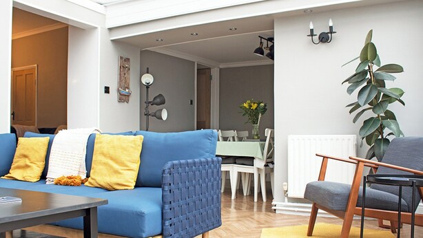 A modern living room with a blue sofa, wooden coffee table, and a dining area with a green tablecloth. - 4 bedroom accommodation in Shanklin (Shanklin)