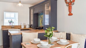 A modern kitchen with a central island, a dining area with white chairs, and a lobster decoration on the wall. - White Horses - UK42776 (Newborough)