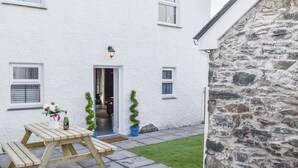 A white building with a stone wall, a wooden table, and potted plants. - White Horses - UK42776 (Newborough)
