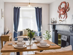 A dining area with a wooden table set for four, a vase with greenery, a fireplace, and a decorative crab on the wall.