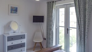 A bedroom with a bed, a dresser with a mirror, a television, and a window with curtains. - Coastal Soul - UK43464 (Lake, near Sandown)