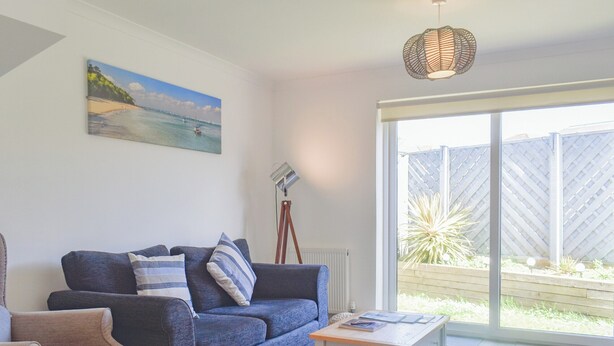 A living room with a blue sofa, a white coffee table, and a painting of a beach scene on the wall. - Coastal Soul - UK43464 (Lake, near Sandown)