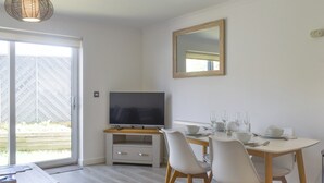 A modern dining area with a TV, white chairs, a wooden table, and a large mirror on the wall. - Coastal Soul - UK43464 (Lake, near Sandown)