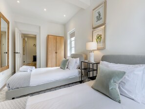 A hotel room with two beds, a bedside table with a lamp, a wardrobe, and framed botanical prints on the wall.