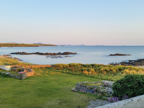 A coastal landscape with grassy areas, rocky outcrops, and a clear view of the sea.