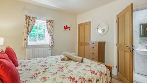 A bedroom with a floral bedspread, a wooden wardrobe, a radiator, and a window with curtains. - Bryn Awelon - UK44122 (Moelfre, near Benllech)