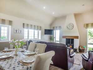 Uma sala de estar acolhedora com lareira, um espaço de jantar com mesa posta para dois e uma área de estar confortável com sofá e cadeiras.