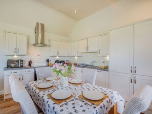 Una cocina moderna con armarios blancos, horno integrado y un comedor preparado para cuatro personas, con una mesa dispuesta para una comida.