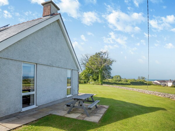 Una casa con techo inclinado, un ventanal grande y un patio con mesa de madera.