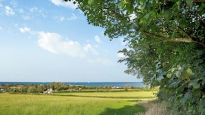 A coastal landscape with a grassy field, trees, and a view of the sea. - Bryn Awelon - UK44122 (Moelfre, near Benllech)