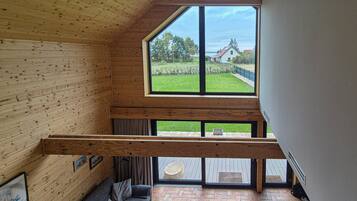 A loft bedroom with a large skylight, wooden beams, a brick floor, and a view of a garden and house.