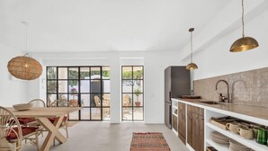Eine moderne Küche mit einem großen Fenster, einem Essbereich mit Korbstühlen und einer hängenden Leuchte.