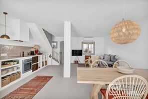 Eine moderne Küche mit weißen Schränken, einem Holztisch und einer gewobenen Pendelleuchte.