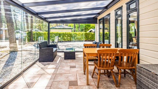 Un patio cubierto con mobiliario exterior, una pared de vidrio y vistas al entorno verde.