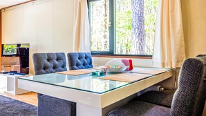Una habitación moderna con una mesa de vidrio, dos sillas tapizadas en azul, un televisor y una ventana con cortinas.