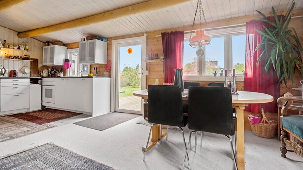A cozy kitchen with white cabinets, a dining area with a wooden table and black chairs, and a large window with red curtains. - 3 bedroom stunning home in Slagelse (Slagelse)