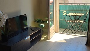 A modern living room with a flat-screen TV, a potted plant, and a balcony with a table and chairs. - Lovely studio in the artists' quarter (Sète)