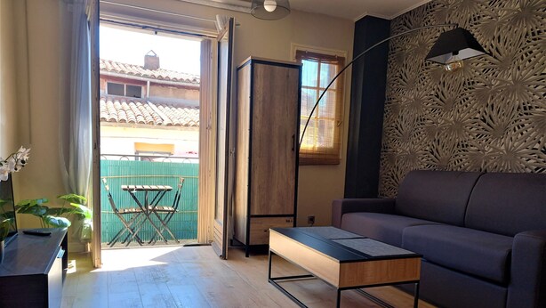 A living room with a sofa, a coffee table, a TV, and a balcony with a table and chairs. - Lovely studio in the artists' quarter (Sète)