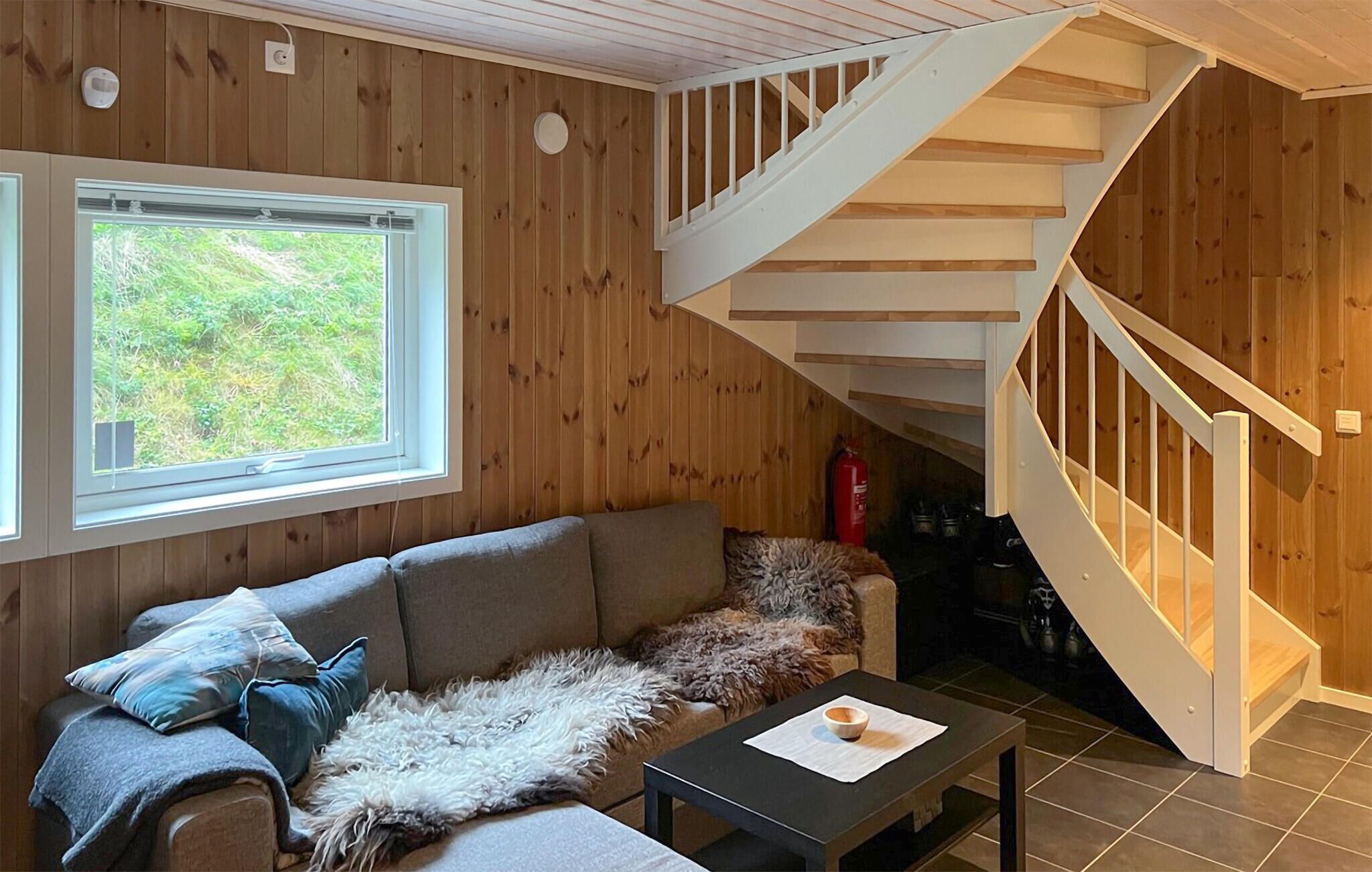 Una sala de estar acogedora con una escalera de madera, un sofá, una mesa de centro y una ventana con vistas a zonas verdes.
