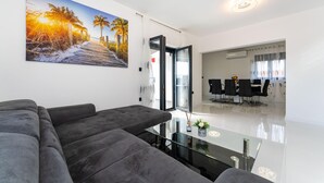 A modern living room with a glass coffee table, grey sofas, and a large beach-themed painting on the wall. - Cozy home in Maslenica (Maslenica)