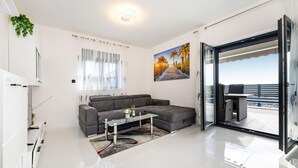 A modern living room with a grey sofa, a glass coffee table, and a view of a balcony with a pool. - Cozy home in Maslenica (Maslenica)