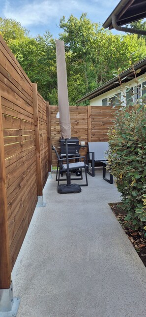 A patio area with a wooden fence, a table with chairs, and a barbecue grill.