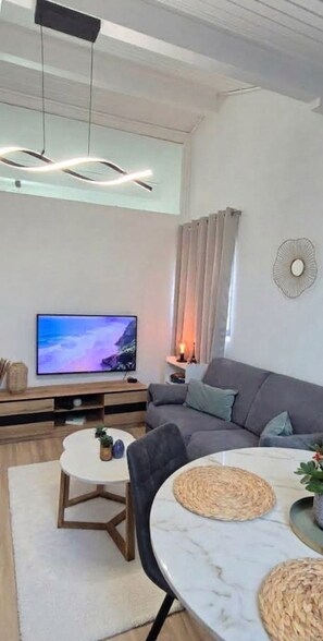 A modern living room with a flat-screen TV, grey sofa, and a dining table with woven placemats.
