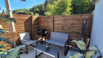 An outdoor patio with a wooden fence, a barbecue grill, and two metal chairs.