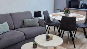 A modern living room with a grey sofa, two round tables, and a kitchen area in the background.