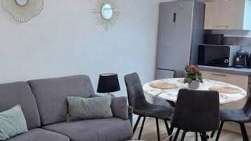Una sala de estar moderna con un sofá gris, dos mesas redondas y una cocina al fondo.