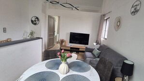 Een moderne woonkamer met een bank, een televisie, decoratieve wandkunst en een eettafel met een bloevas.