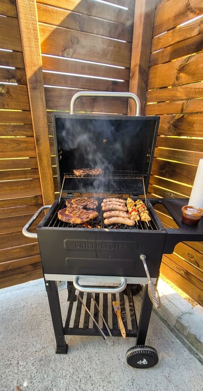 A GRILLMEISTER barbecue grill with multiple cooking grates and a chimney, set against a wooden backdrop.