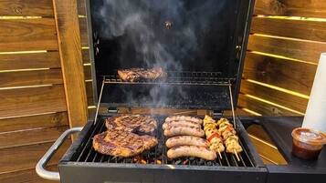 A GRILLMEISTER barbecue grill with multiple cooking grates and a chimney, set against a wooden backdrop.