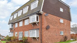 A two-story brick apartment with multiple windows, a satellite dish, and a small garden area.