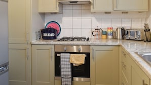 A kitchen with beige cabinets, a stove, a toaster, and a pot labeled 'BREAD'.