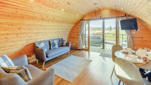 A cozy cabin interior with a wooden ceiling, a sofa, a dining table with chairs, and a TV mounted on the wall. - This luxury lodge with a private hot tub is perfect for exploring Mid Wales. (St Harmon, near Rhayader)