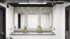 A modern bathroom with three sinks, two mirrors, and potted plants.